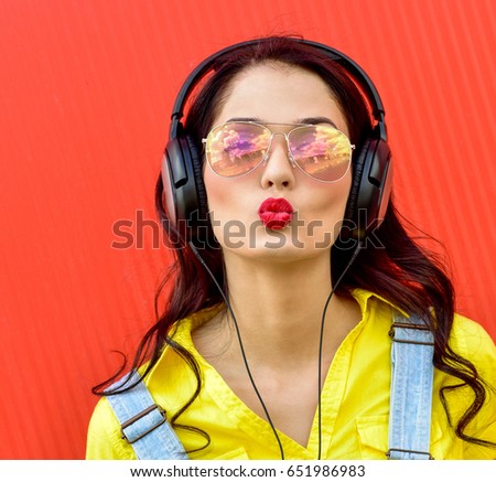 Beautiful smiling woman with headphones listens to music over red background.  Fashion woman in sunglasses outdoor.