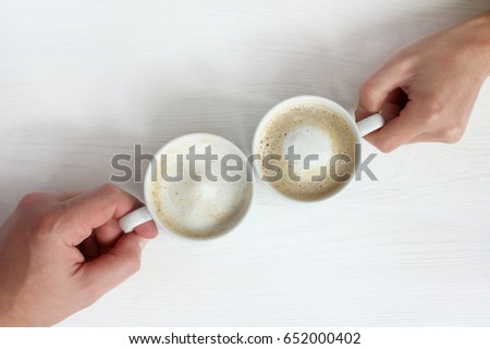 Two cups with frothy cappuccino in hands/ coffee break in a top view
