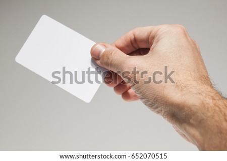 Male hand with white empty card over gray wall background, close-up photo with selective focus