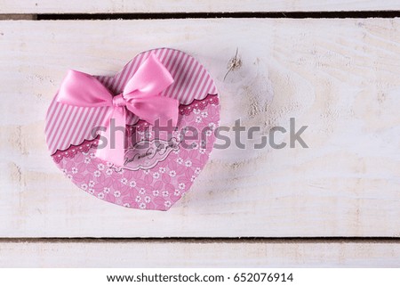 Pink color heart shaped box with pink bow above wooden background.
