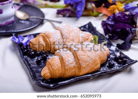Breakfast with sweet croissants and coffee on black plate surrounded with iris flowers in bed. Good morning concept. Selective focus, close up.