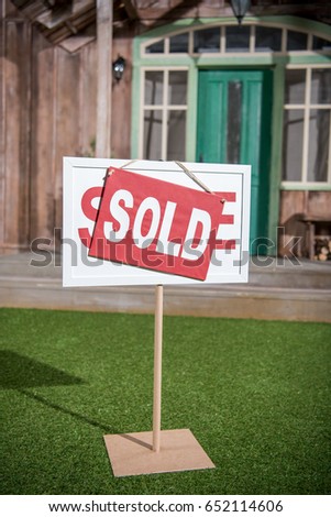 sale banner with sold card standing near new house 