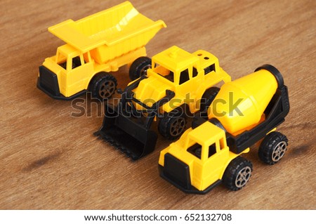 Group of small heavy construction machine toy, lorry, bulldozer and concrete mixer. All made of plastic isolated on a wood grain texture background.