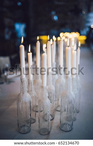 White candles in bottles of wine stand on white table