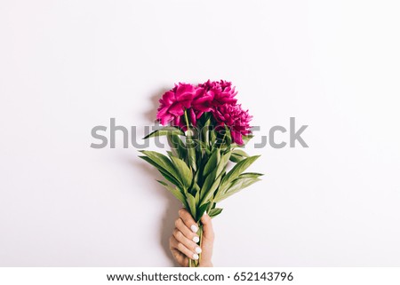 Bouquet of red peonies in a female hand with a manicure on a white background, close-up