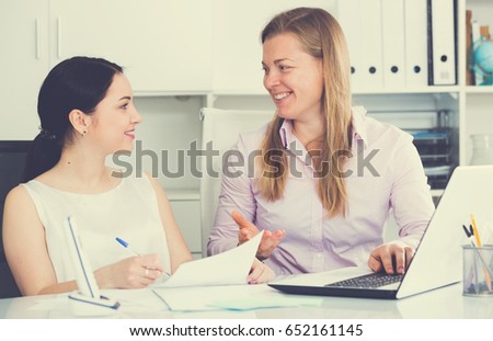 Two young female workers working productively on project in office