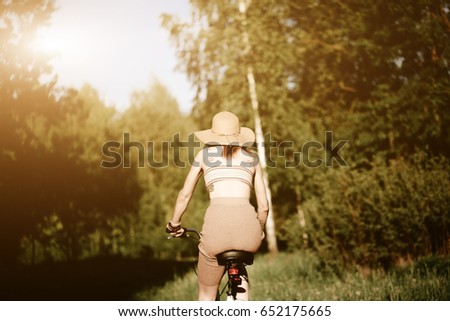 Funny girl driving bicycle outdoor. Sunny summer lifestyle concept. Woman in dress and hat in Field with dandelions. Female ride in park. Light photo effect for text. Copyspace for design