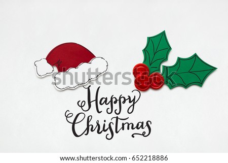 Creative photo of santas hat and holly berry made  of paper on white background.