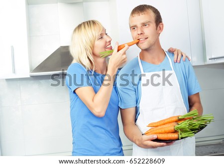 beautiful happy young couple with carrots in the kitchen at home