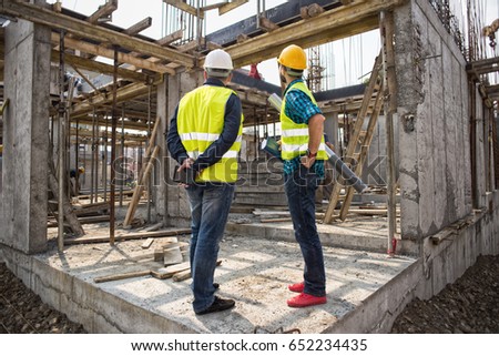 Men in hardhat and green jacket posing on building site.Film noise
