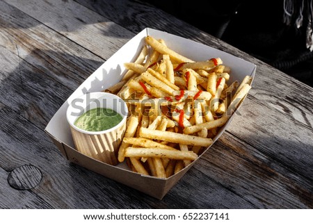 Fries with ketchup and guacamole dip on the side on a wooden plank