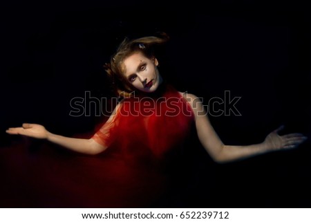 Underwater portrait ot young beautiful girl with make up in red stylish dresses in the swimming pool