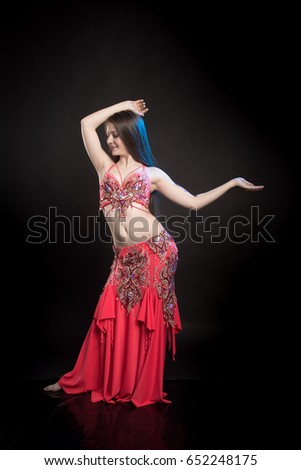 Dancer girl brunette with long hair in red oriental costume and mehendi on hand posing and dancing on black background in studio