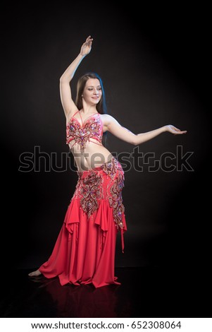 Dancer girl brunette with long hair in red oriental costume and mehendi on hand posing and dancing on black background in studio