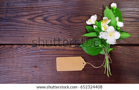 bouquet of blooming white jasmine with an empty paper tag on a brown wooden table, top view, empty space