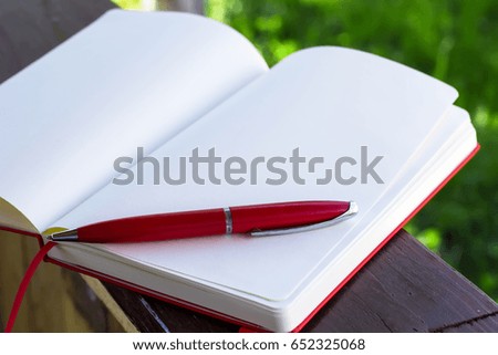 Red notebook for notes and a pen on the background of a sunny summer day