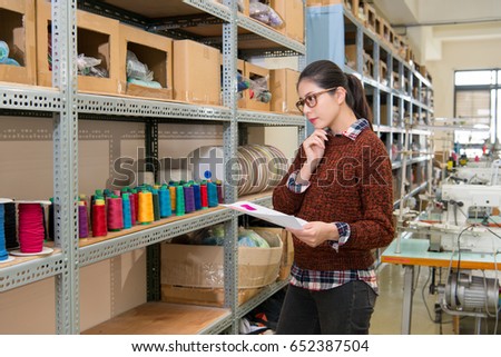 beauty smiling clothing tailor woman standing in front of color spool thread collection cabinet thinking which reel correct in fashion sewing studio.