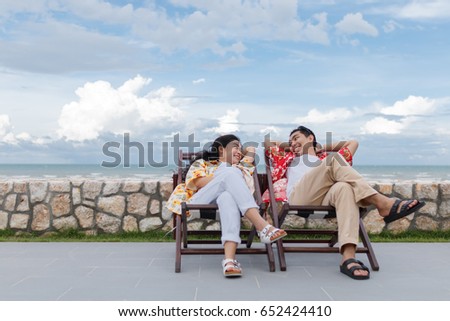 couple asian man and woman with yellow and red shirt sitting, beautiful sky background Royalty-Free Stock Photo #652424410