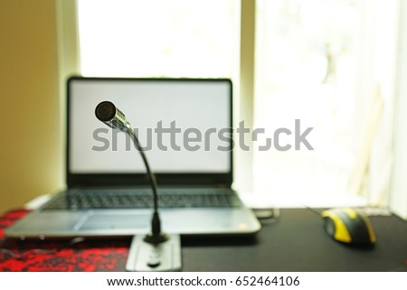A computer notebook , microphone and a yellow gaming mouse are set up on a large gaming mouse pad near a window. 