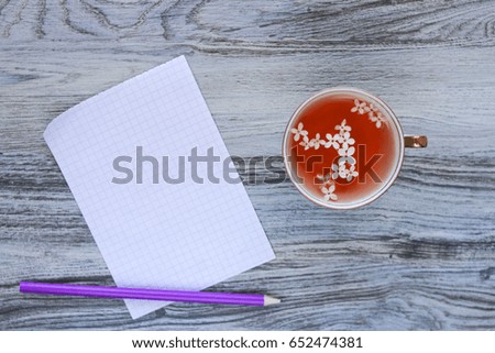 A fragrant vitamin home herbal tea with white lilac flowers and a sheet of clean white checkered paper with a purple pencil on a wooden aged gray background.