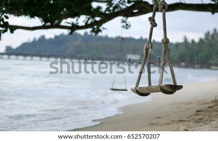 Swing hanging from a tree on the beach with a wave in the background