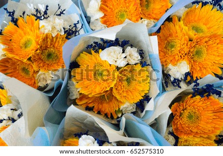 Fresh flowers in outdoor flower market. Yellow gerberas and white carnations in white blue paper wrap.