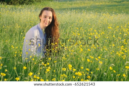 Young woman in blue top sitting in field of wildflowers