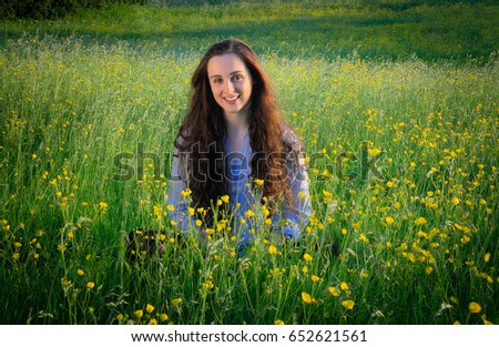 Young woman in blue top kneeling in field of wildflowers