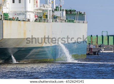 Tanker discharging ballast into the harbor. Water flows from the side. Ship not identifiable. Only part of ship visible. Royalty-Free Stock Photo #652624141