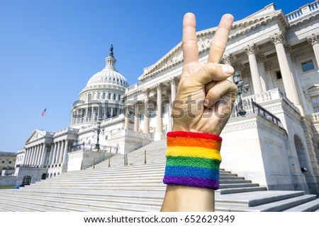 American hand wearing gay pride rainbow flag wristband holding up a peace sign gesture in front of the Capitol Building in Washington, DC, USA