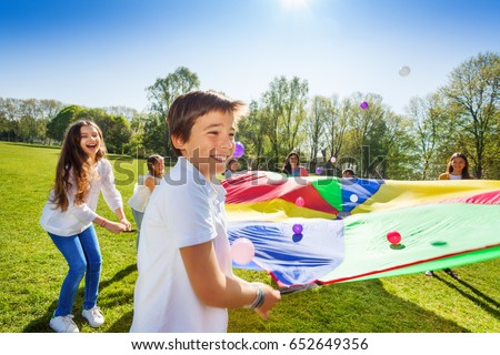 Boy throwing balls up by using rainbow parachute Royalty-Free Stock Photo #652649356