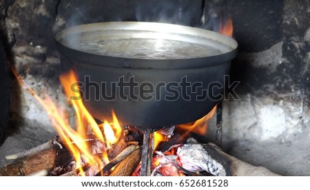 man cooking food in a pot on the fire, cover pan with a lid, the tourist camping, outdoors