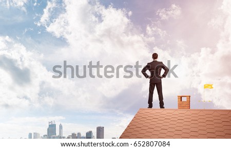Young determined businessman standing on house roof and looking away. Mixed media