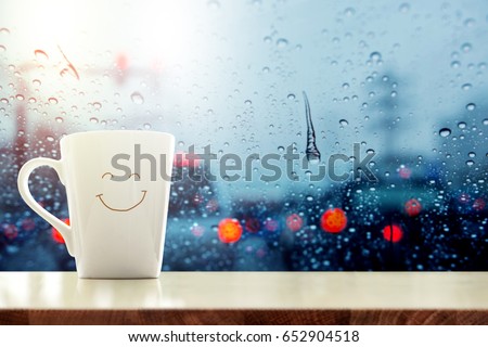 Happy Coffee Mug with smiley face on desk inside glass window, Blurred traffic jam light in city as outside view, Relaxing in cafe or Rest on rainy day