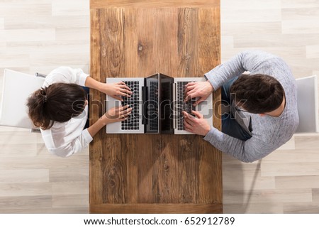 Overhead View Of Couple Sitting Face To Face Using Laptop On Table Royalty-Free Stock Photo #652912789
