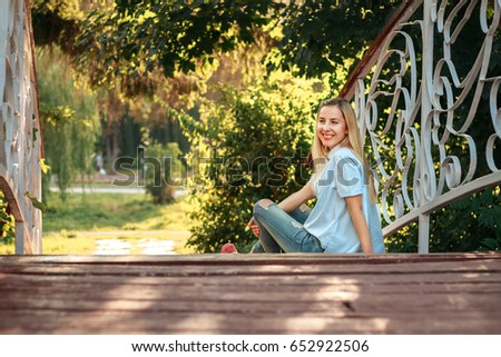 Happy young girl sitting on wooden bridge.