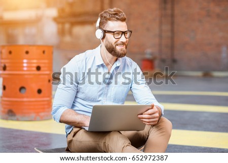 Handsome hipster businessman working with laptop sitting on the skateboard on the rooftop background. Lifestyle business concept