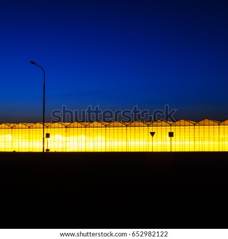 Greenhouse plant at night. Night landscape luminous glass construction. Silhouette of road signs on a background of a facade of a hothouse