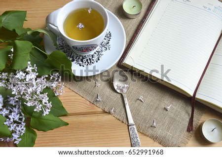 Cup of tea, teaspoon, diary, candles and lilac flowers with vintage napkin on wooden background