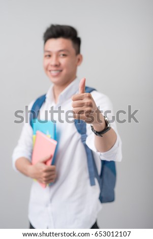 Asian male student making a thumb up sign isolated on gray background