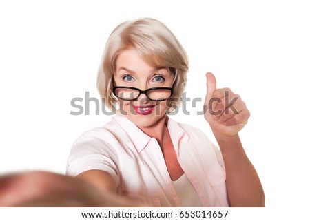 Beautiful blond elderly woman with glasses makes selfie and shows thumb over a white background