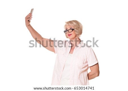 Beautiful blond elderly woman with glasses makes selfie over a white background, space for text