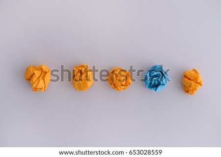 Four crumpled yellow paper balls and one blue on a grey background. Idea concept.