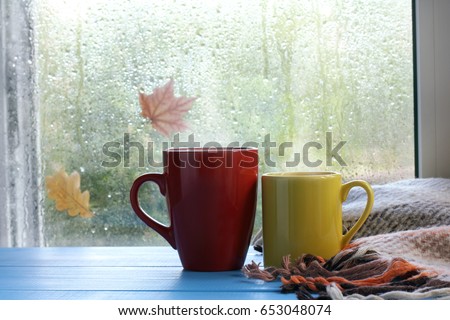 two cups and a blanket against the window with rain drops and leaves / warming the atmosphere in the rainy time
