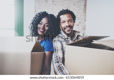 Closeup view of young black african man and his girlfriend moving boxes into new house together and making a successful life.Cheerful family standing in empty new apartment.Blurred background