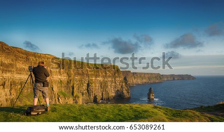 tourist with camera taking epic views from the cliffs of moher in county clare ireland. ireland's number 1 tourist attraction. beautiful scenic irish countryside landscape along the wild atlantic way.