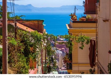 The neighborhood called Quartieri Spagnoli in Naples, Italy. Street view of old town. Narrow street of Napoli. Bright sunny day. Gulf of Naples, blue sky, sea on background. Cacti on the terrace. Royalty-Free Stock Photo #653095996