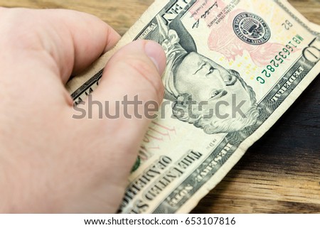 a picture of a Caucasian hand holding a ten USA dollar note on a wooden background.  This image can be used to represent payment or money.