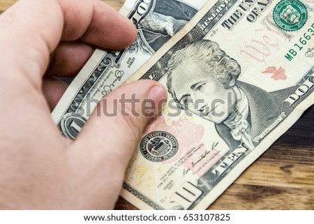 a Caucasian hand holding USA dollars on a wooden background.  This image can be used to represent payment.