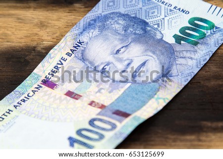 A South African hundred rand note on top of a wooden table. This image can be used to represent payment or money. 